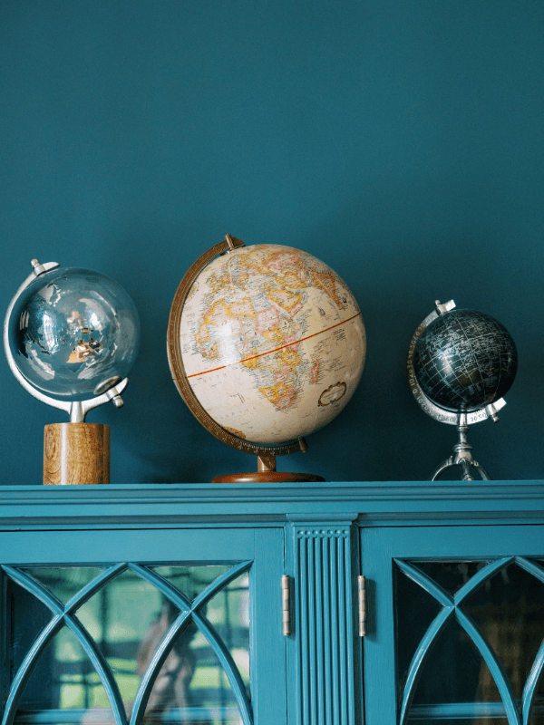 Three vintage globes — cream, metallic blue, and black celestial — displayed atop the teal Gothic arch bookcase in Bohemia Manor Farm's library.