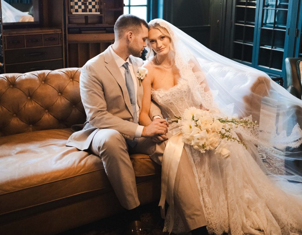 A newlywed couple sitting next to each other on a leather Chesterfield couch in Bohemia Manor Farm